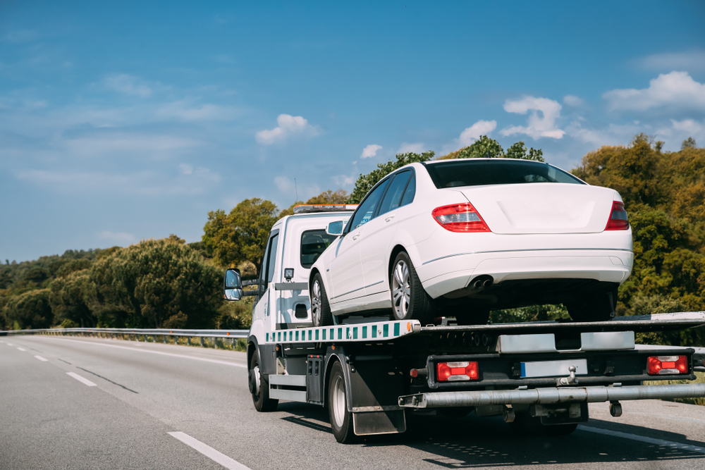 white car being towed by a tow truck on a busy highway.